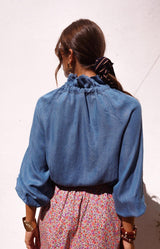 Soft denim blue blouse with a romantic ruffle neckline and elegant tie detail in fluid fabric – Volange Paris, Parisian fashion in Sydney (Mosman, Paddington and Bronte) or Australia-wide online.