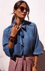 Soft denim blue blouse with a romantic ruffle neckline and elegant tie detail in fluid fabric – Volange Paris, Parisian fashion in Sydney (Mosman, Paddington and Bronte) or Australia-wide online.